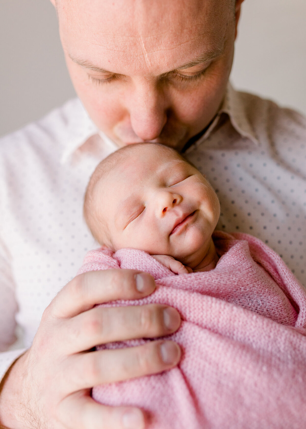 Dad holding swaddled baby girl in pink in white studio. Image captured by Brandon, Mississippi photography.