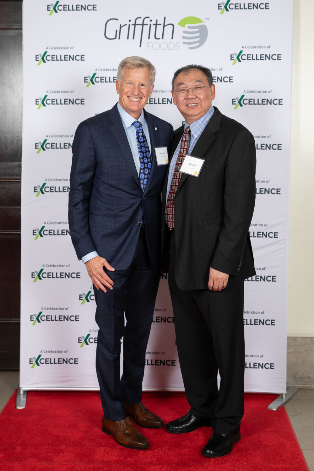 Two men posing in front of an "Excellence" step-and-repeat banner