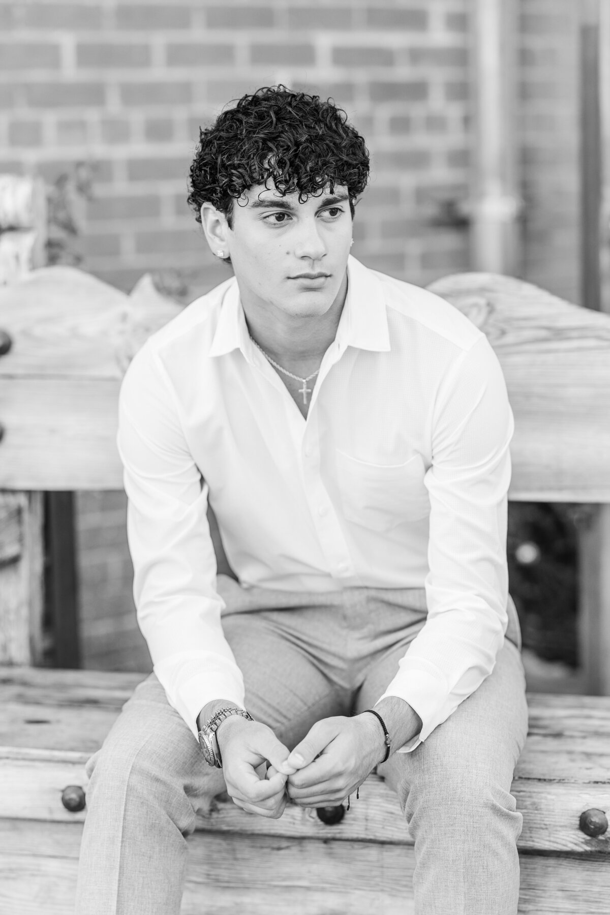 A striking black and white senior portrait of a young man seated on a rustic bench in the Fort Worth Stockyards. Captured with a timeless editorial flair by Jennifer Lynn Photography.