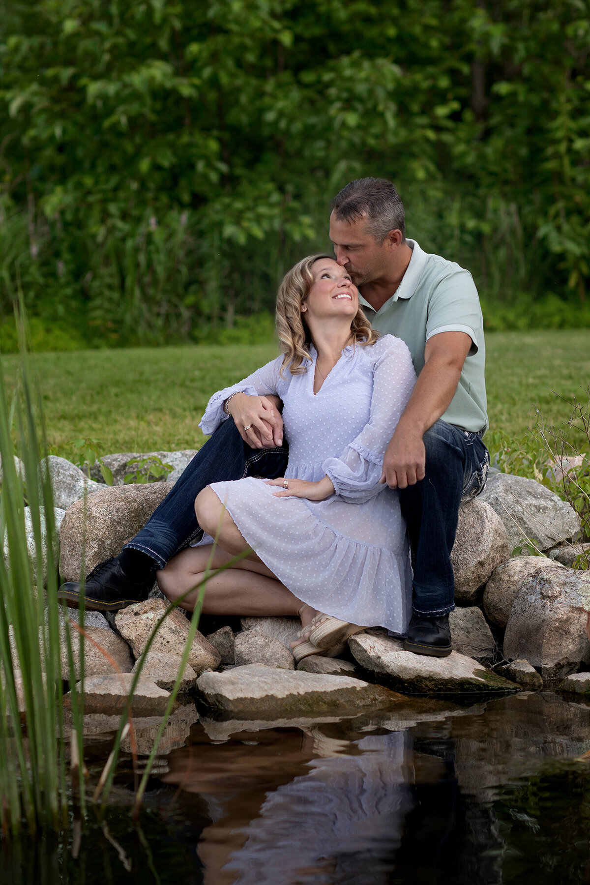 Dad kisses Mom as they sit on the rocky edge of a pond