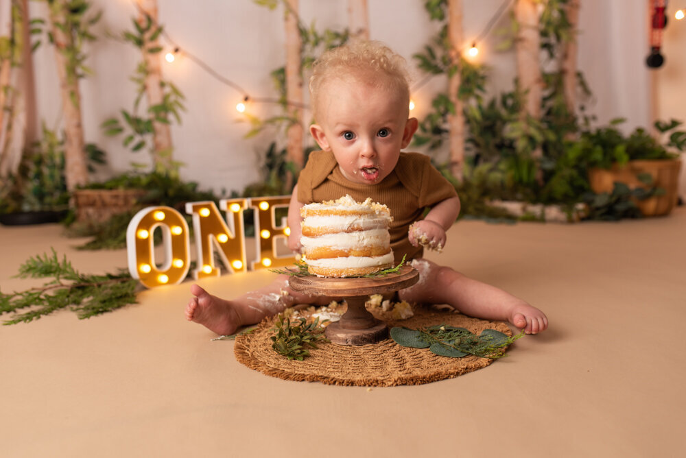 Photo shoot with Atlanta, Georgia cake smash photographer photographing one year old baby boy at marietta ga portrait studio eating smash cake in a forest themed set up
