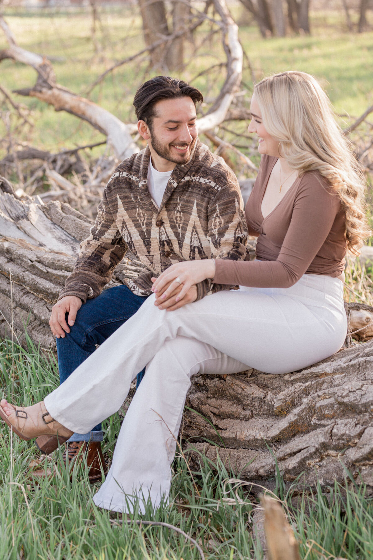 An engaged couple sits on a fallen tree beside Boulder Creek