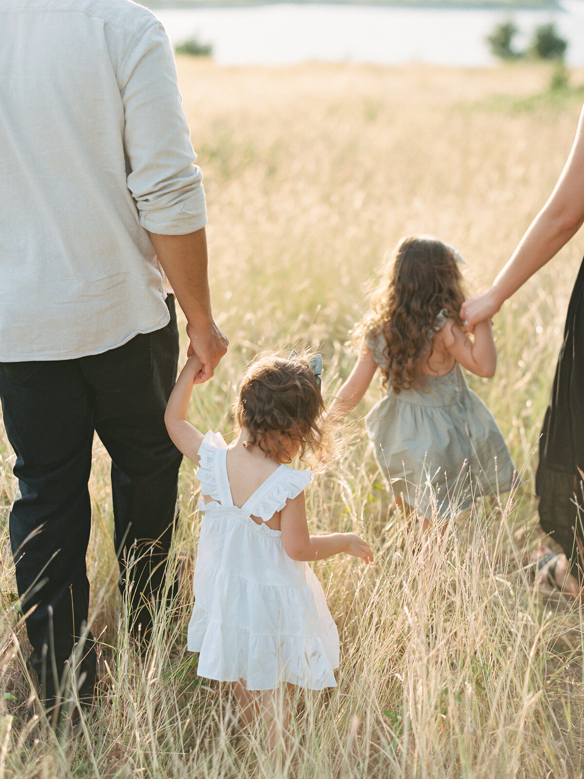 Parents and their two daughters holding hands and walking through a grassy field