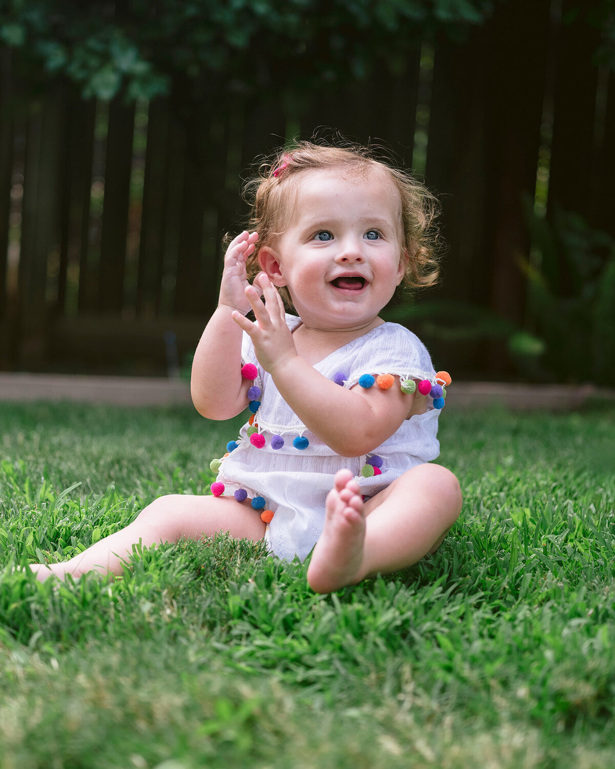 Portrait of a baby clapping while sitting on grass during a first birthday party in the Bay Area, captured by a San Francisco Bay Area first birthday photographer.
