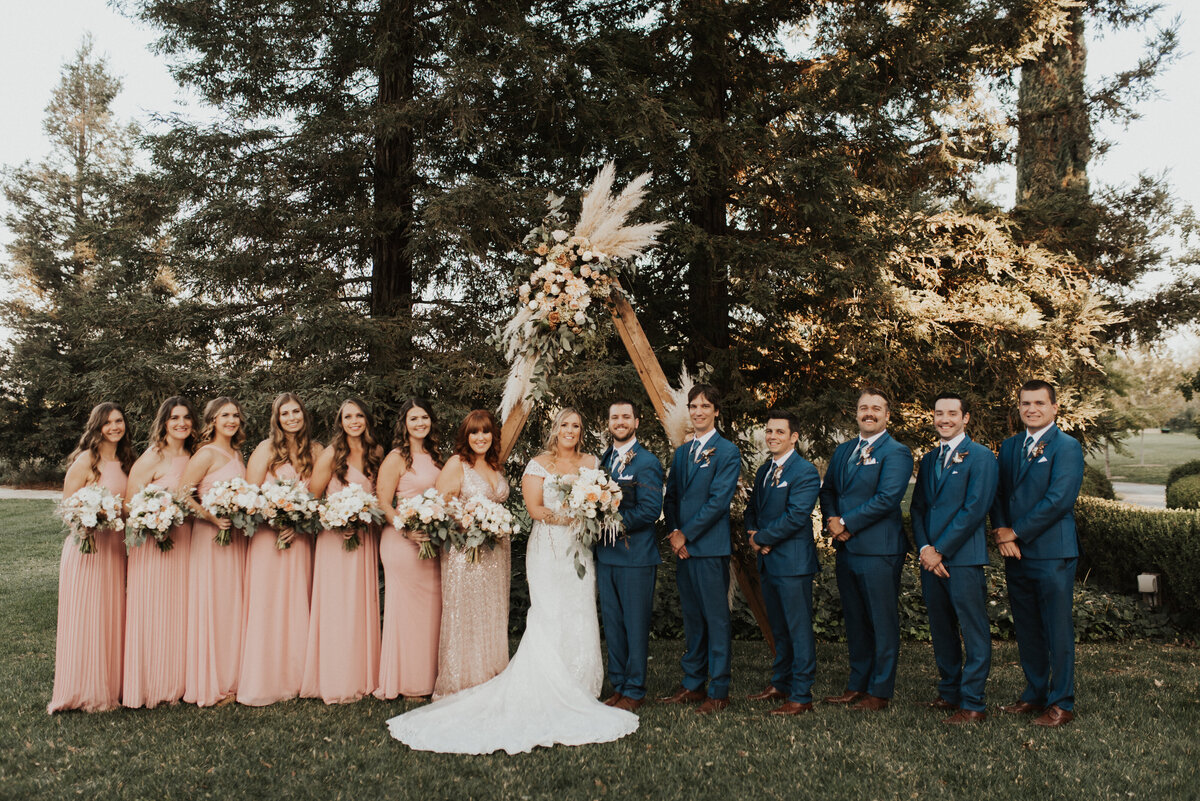 wedding party in blush dresses and pink suits smiling at the camera