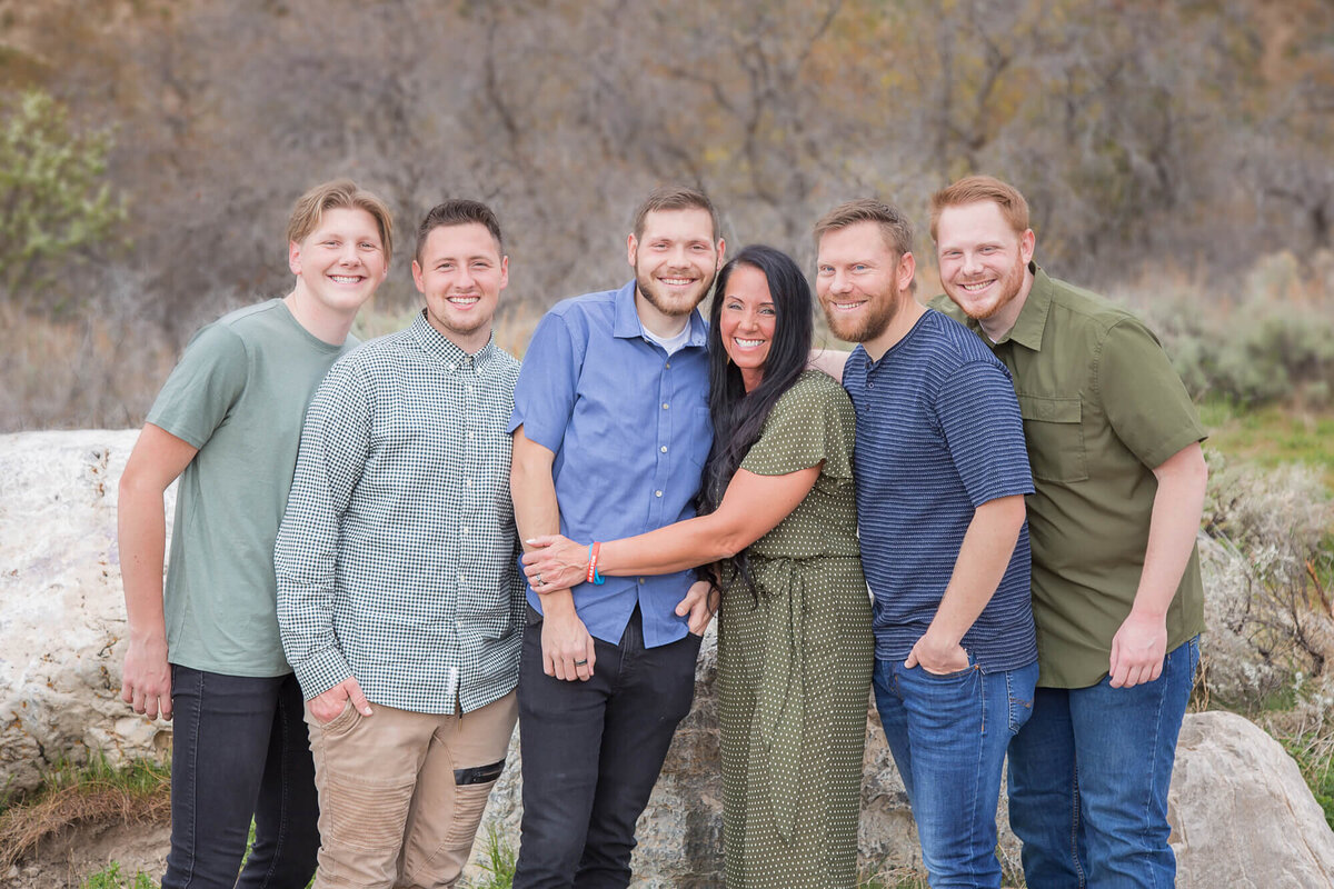 Dark brown haired woman with five sons, all wearing blue and green at a mountain park