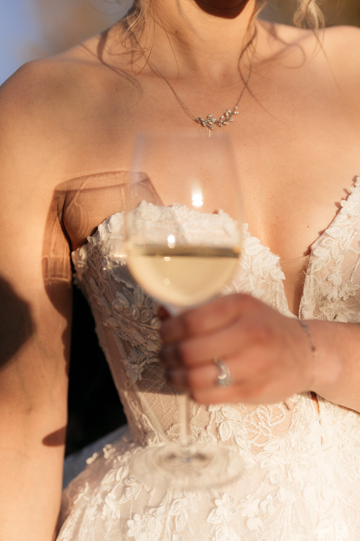 bride holding glass of white wine at sunset