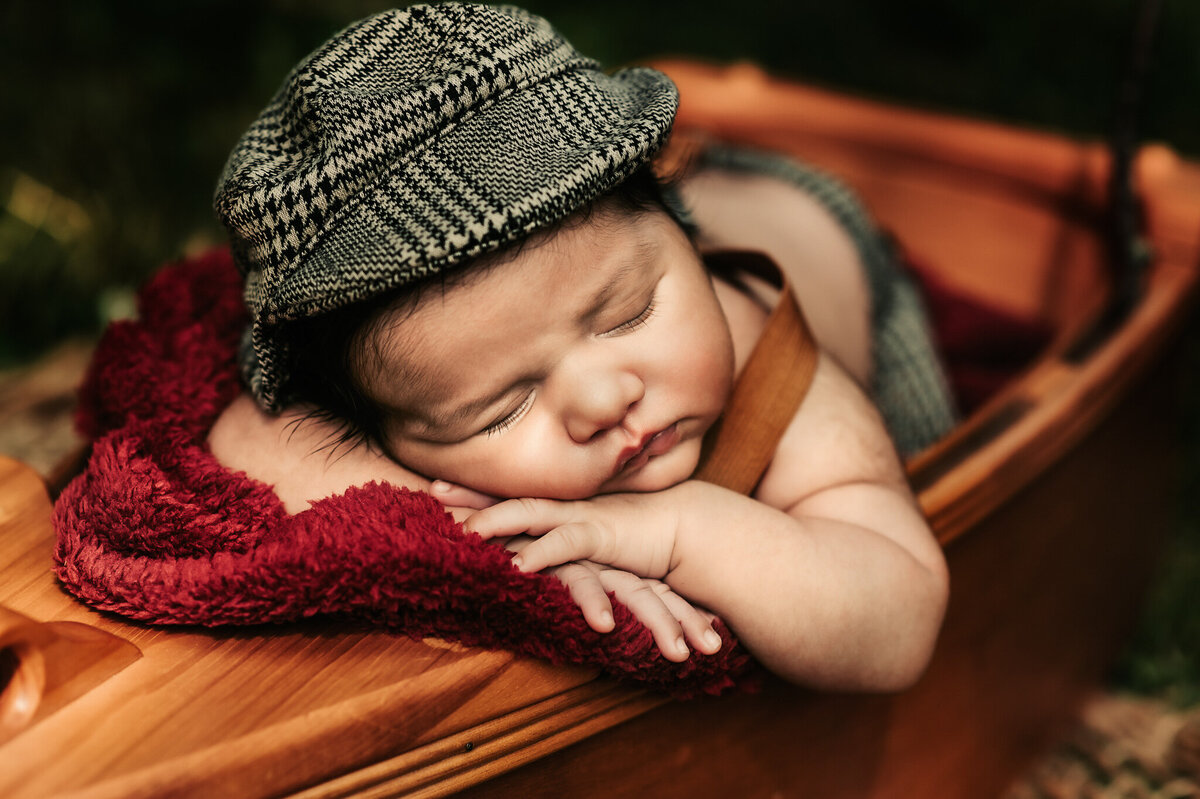 Baby boy wearing a checkered hat asleep in a canoe at his outdoor photography photoshoot by Tamara Danielle.