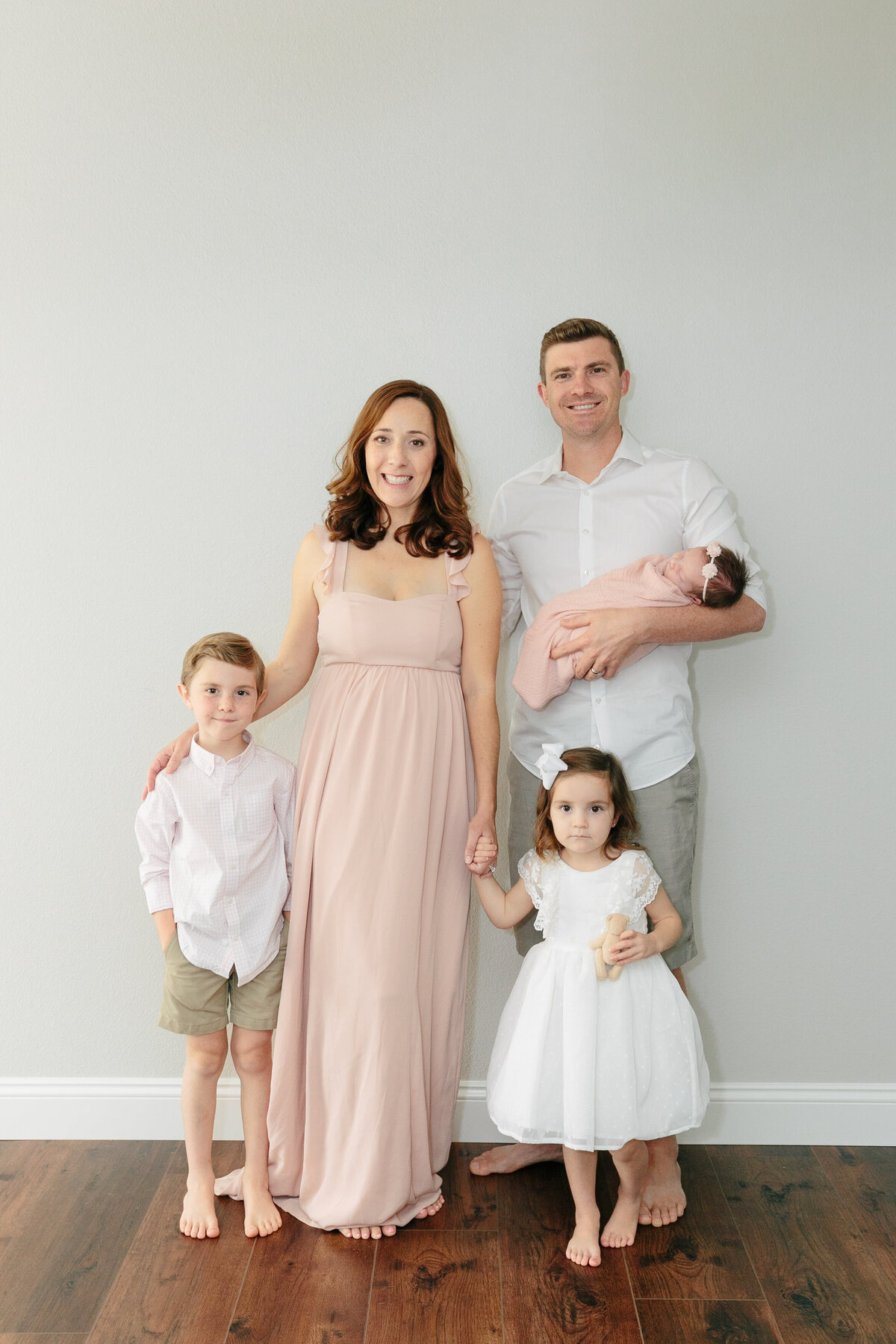 A mom holding two kids hands while she stands next to her partner holding a newborn
