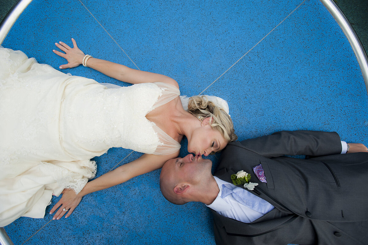 A newlywed couple laying down in opposite directions kissing 