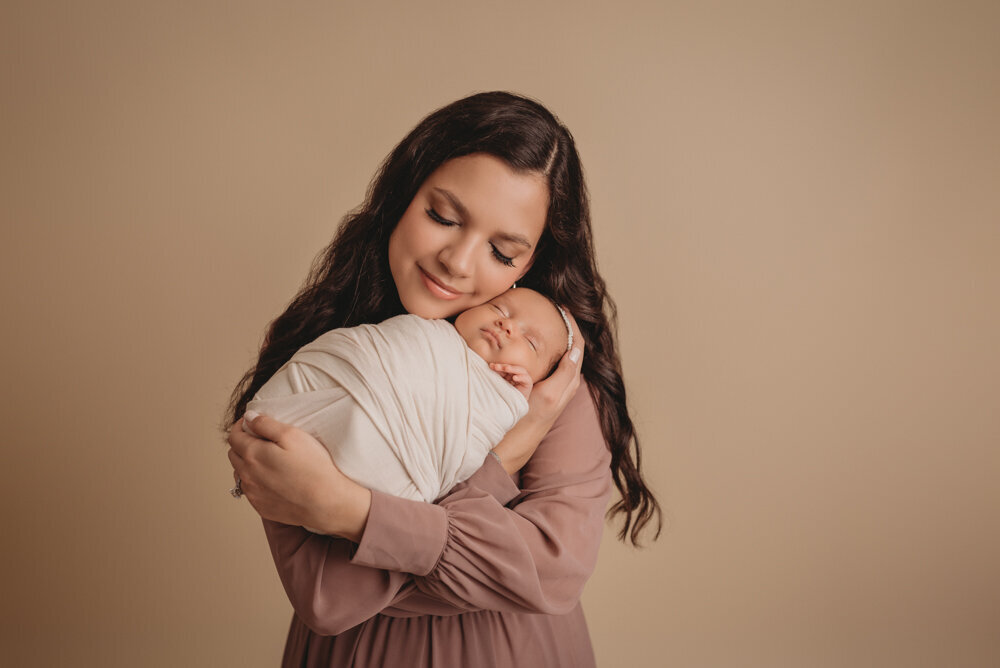 Mom and baby posing together for newborn session at Atlanta, Georgia newborn photographer studio. Mom is snuggling baby closing her eyes.