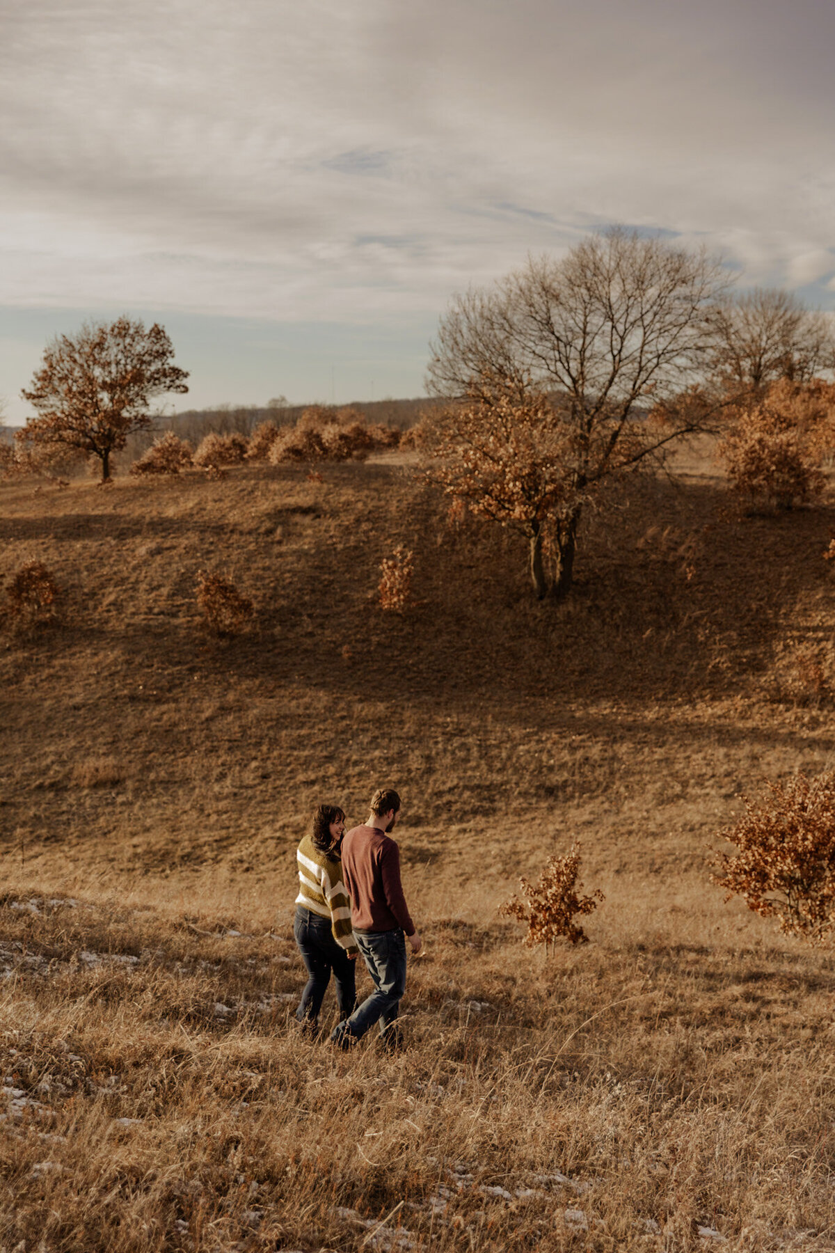 Engaged couple walking in a field of grass captured by a Minnesota Couples Photographer