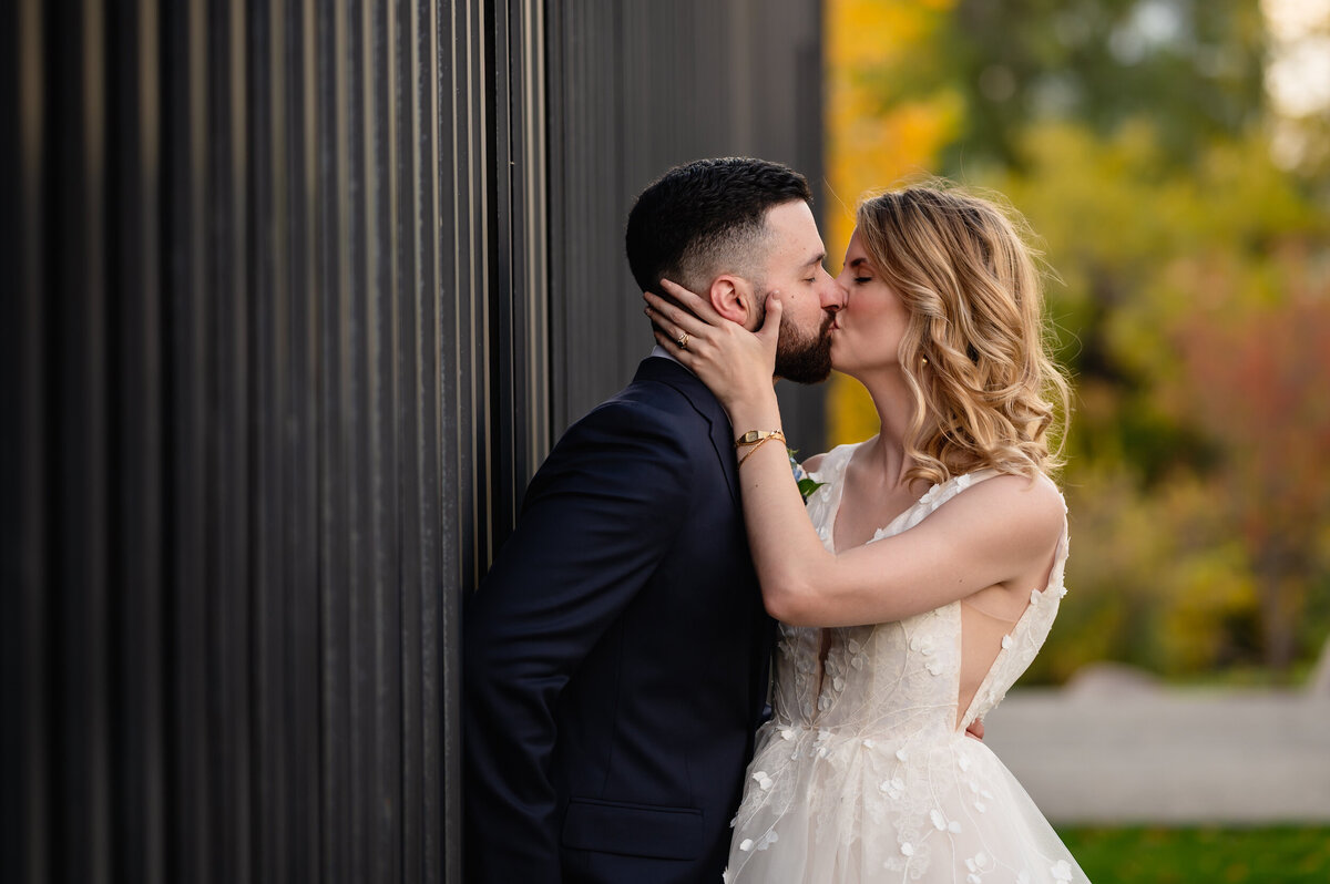 Groom and bride kiss in front oof a black wall
