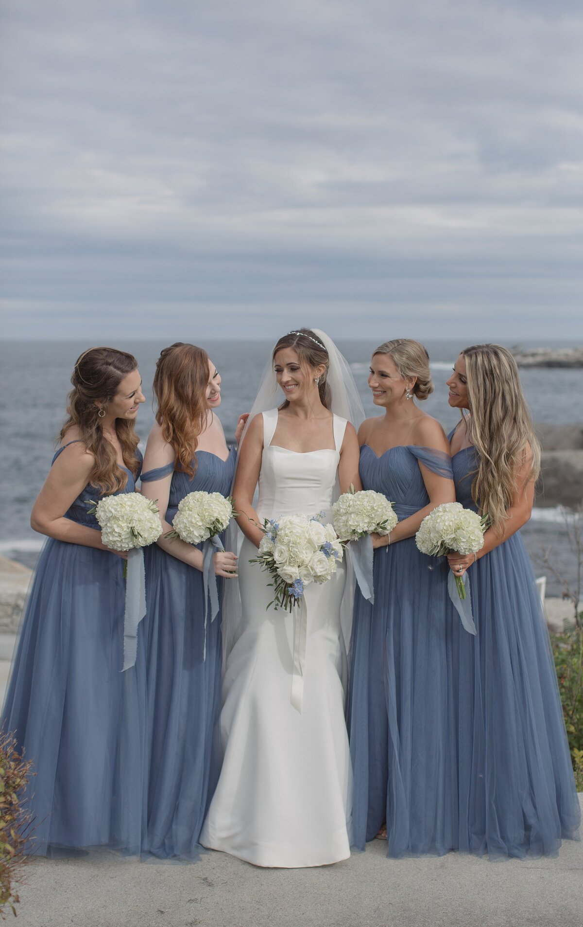 Bridesmaid pose with bride in baby blue dresses with Atlantic Ocean behind them.
