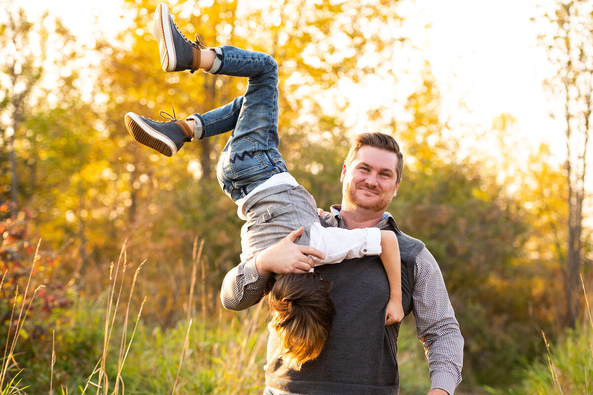 a father hangs his son upside down playfully during their family photos in Ottawa