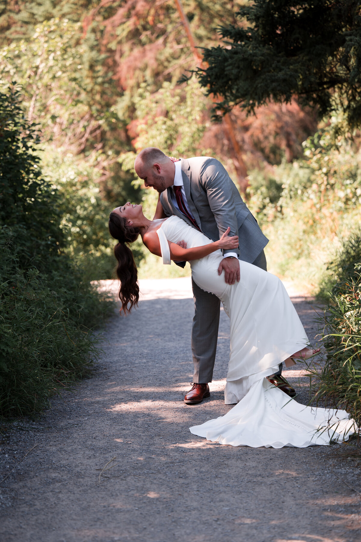 wedding couple do a dip and kiss on a pathway in the park