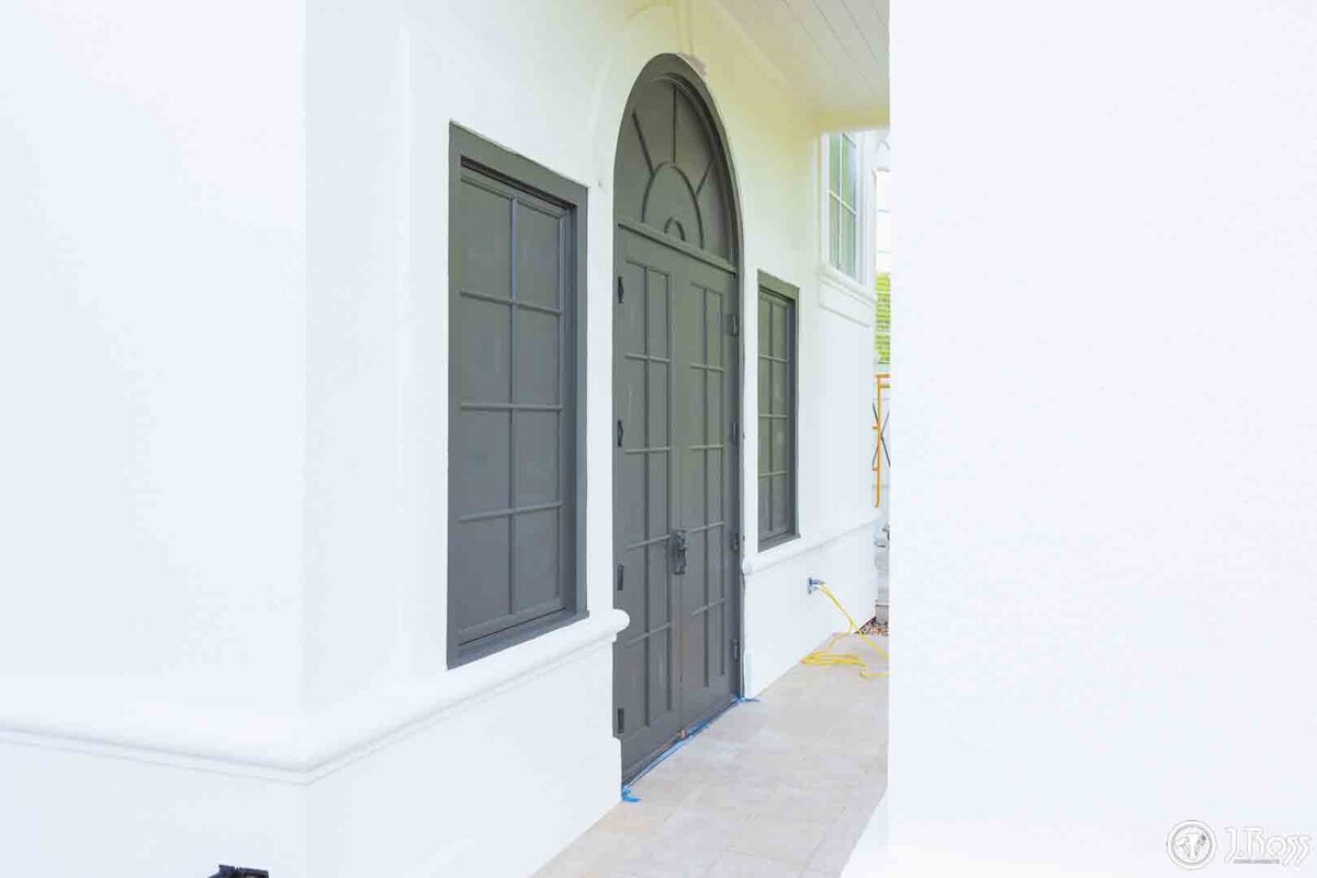 View of a narrow walkway where a dark arched door and side windows contrast sharply with the freshly painted white stucco walls and trim, highlighting detail-oriented home exterior painting Bristol, VA.