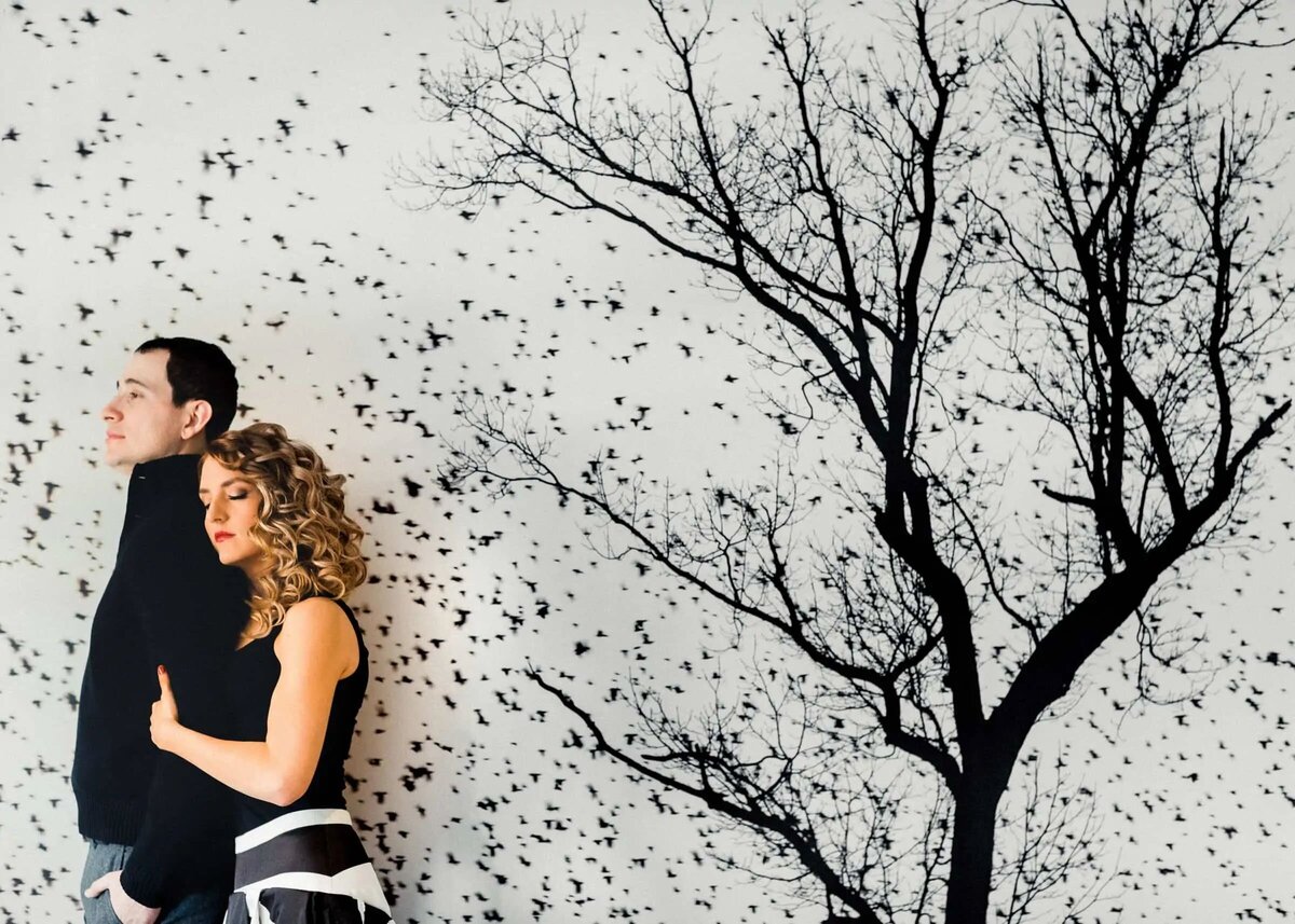 Vibrant image of a couple back-to-back against a wall with a dramatic black and white tree mural