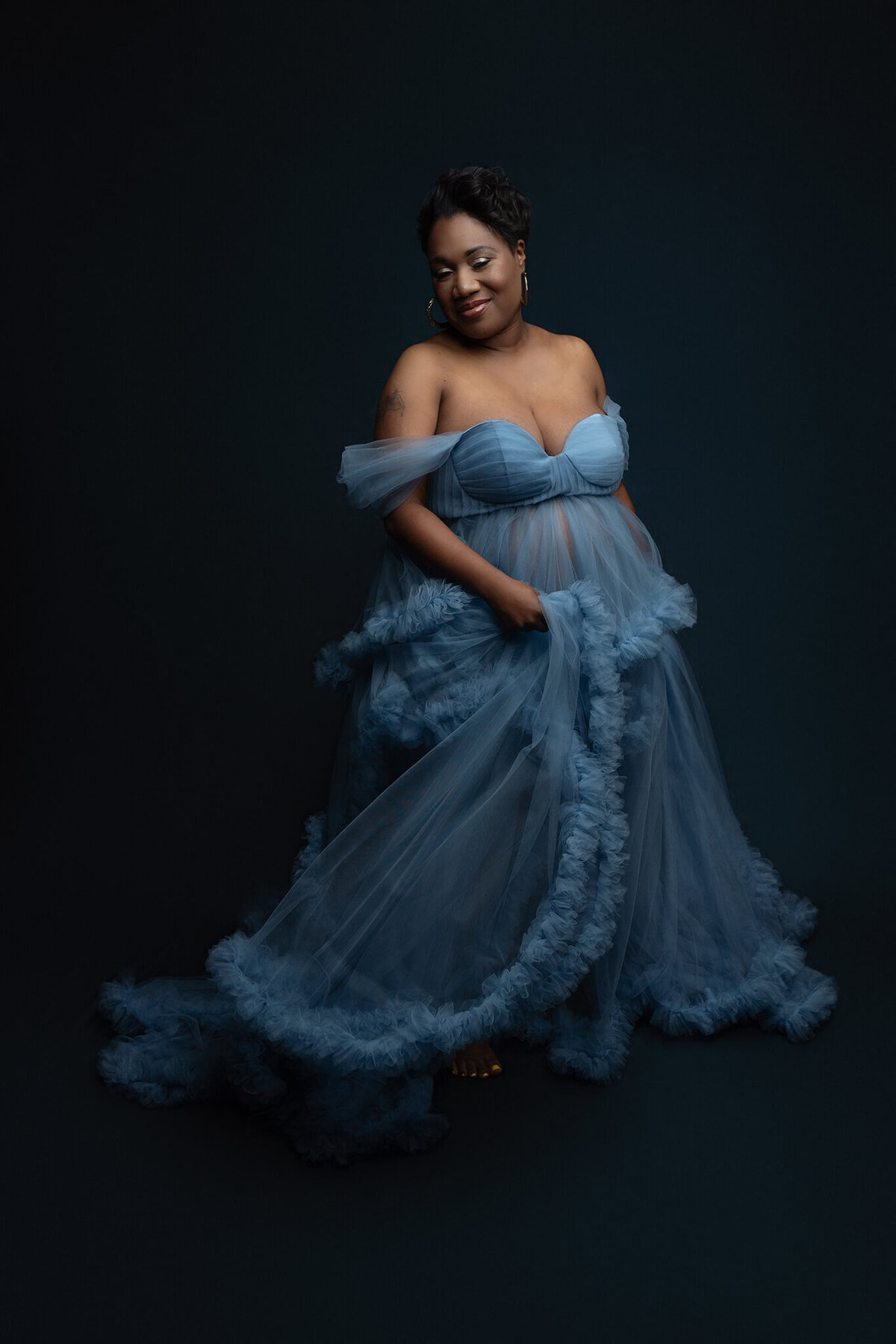 A woman in a blue tule maternity gown smiles and twirls for a New Orleans Maternity Photographer