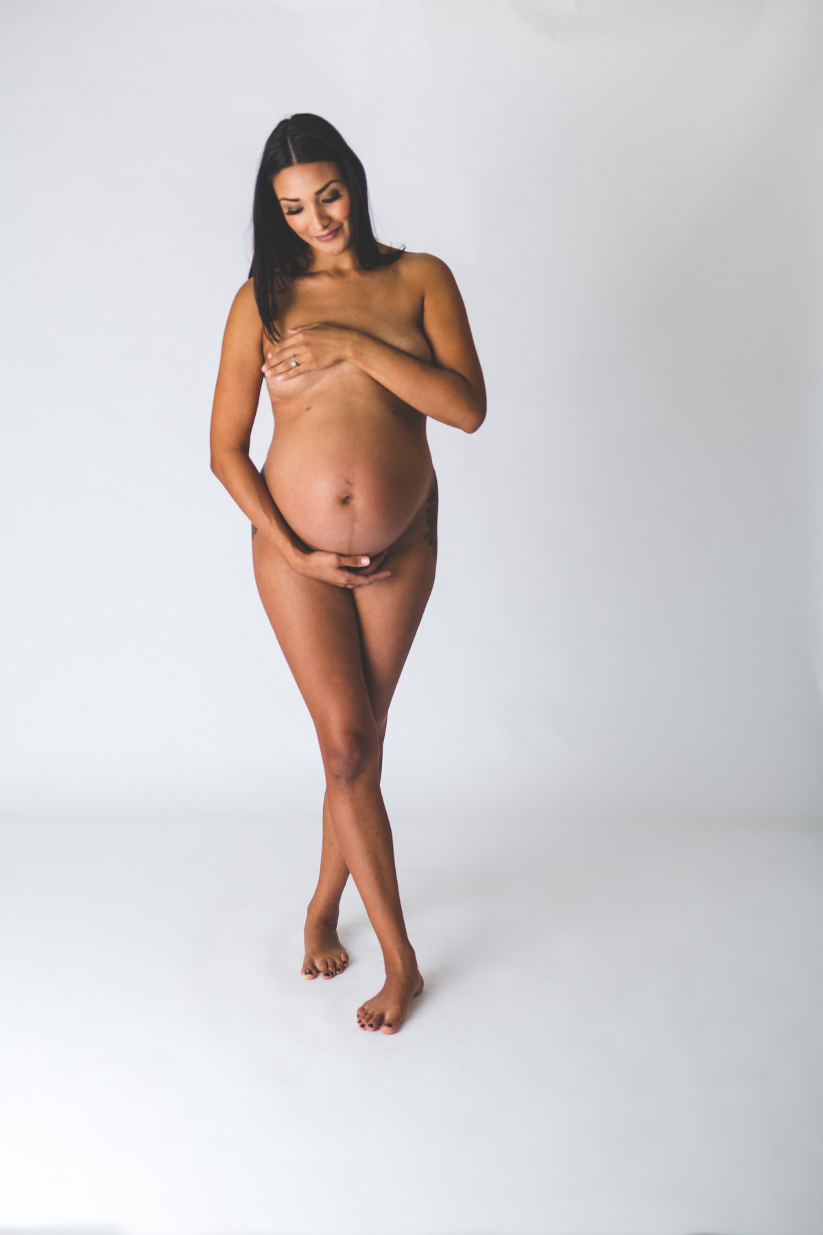 San Antonio Maternity photography session of dark haired woman covering herself with her hands and holding her belly.