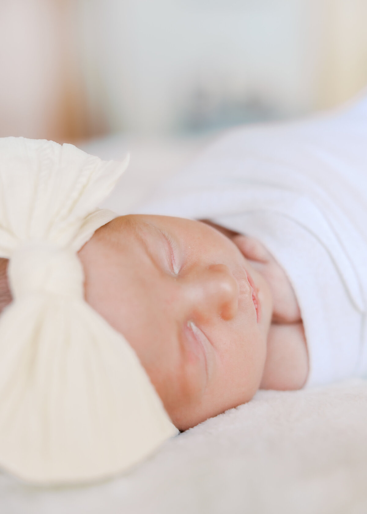 Newborn baby is swaddled with big cream bow for her newborn photography session in chanhassen, mn with angela watts photography.