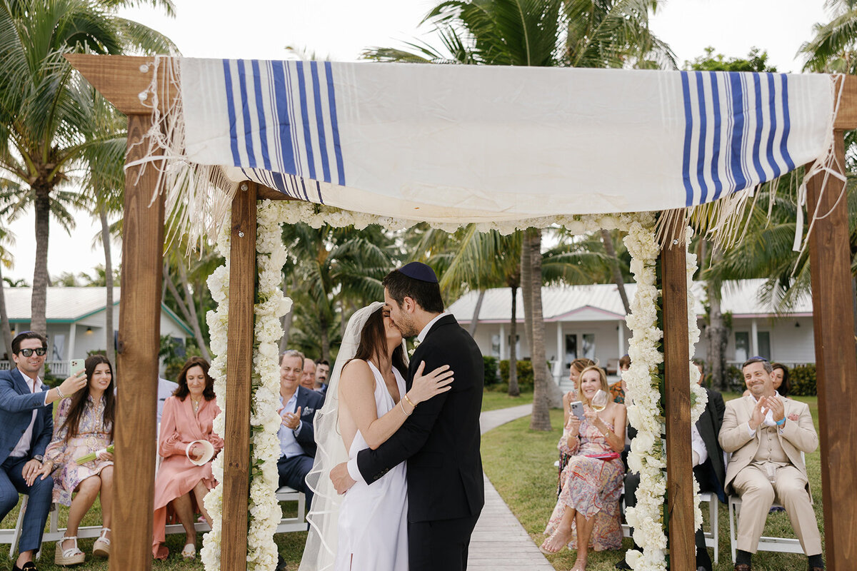 An intimate moment as the couple stands beneath the chuppah, surrounded by friends and family. Florida Keys destination wedding photography by Claudia Amalia.