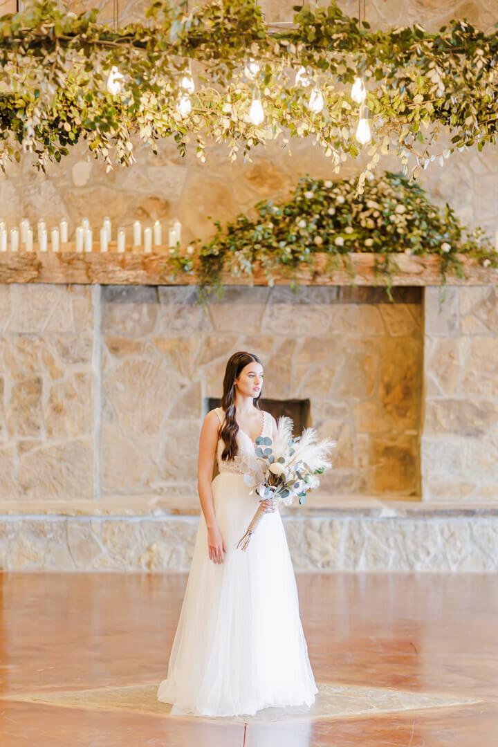 A bride walks in a large open stone walled room holding her bouquet