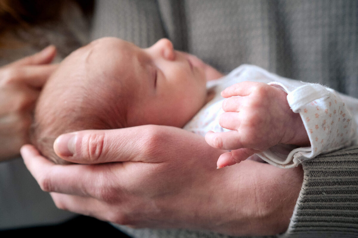 Close-up of a newborn baby resting in an adult’s hands, eyes closed, peaceful and still.