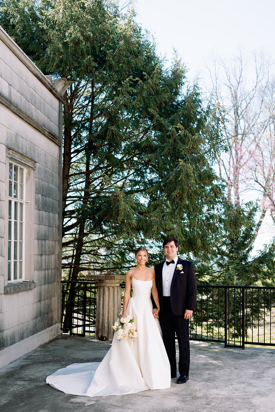 Bride and groom standing together, holding hands and smiling on the terrace at Burritt on the Mountain in Huntsville, Alabama, photographed by Perry Hancock.