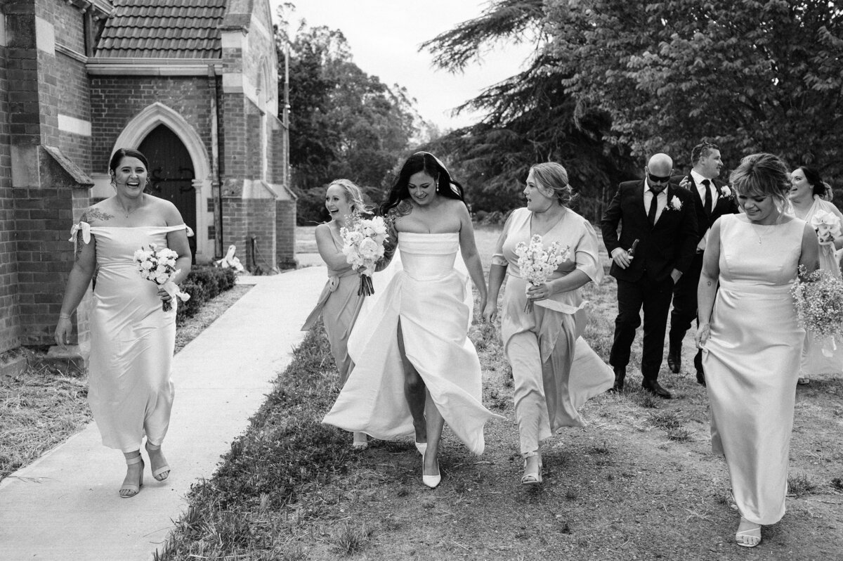 candid photo of bridesmaids and bride walking alongside a church