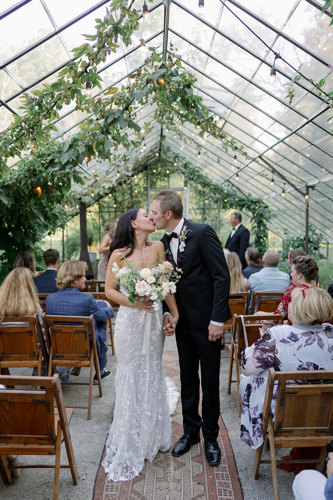 Bride and groom kissing during their recessional inside the greenhouse at Glasshouse Community, a popular Michigan wedding venue.
