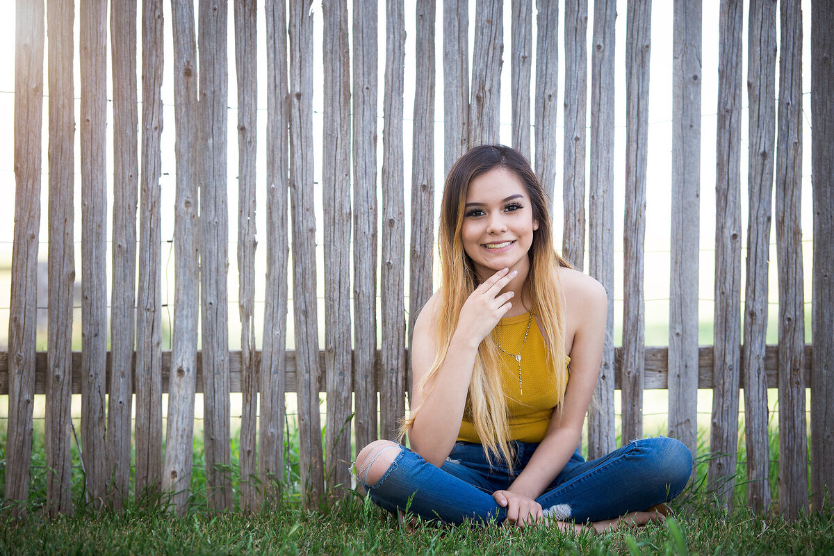 senior girl sitting against wooden fence