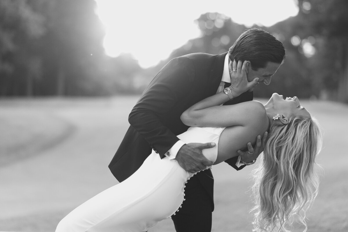 Black and white of groom dipping his bride at sunset