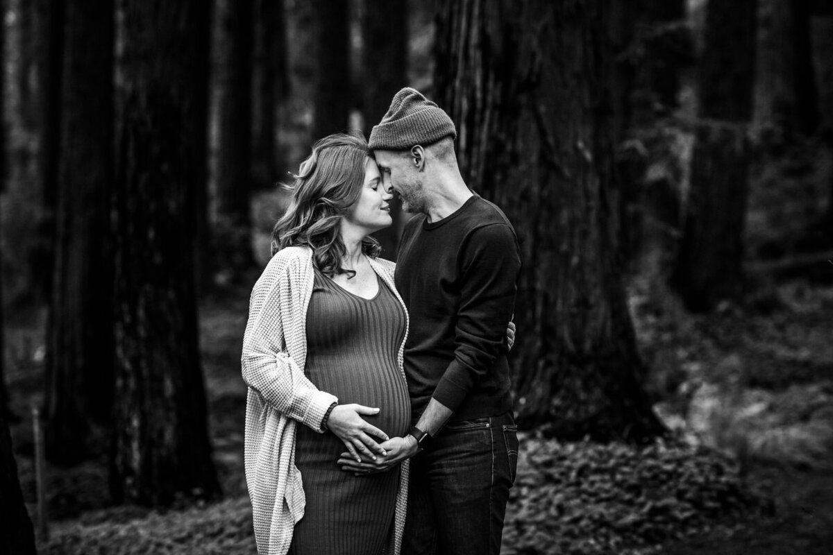 pregnant woman touching foreheads with her husband with both of their hands on her bump in Berkeley garden