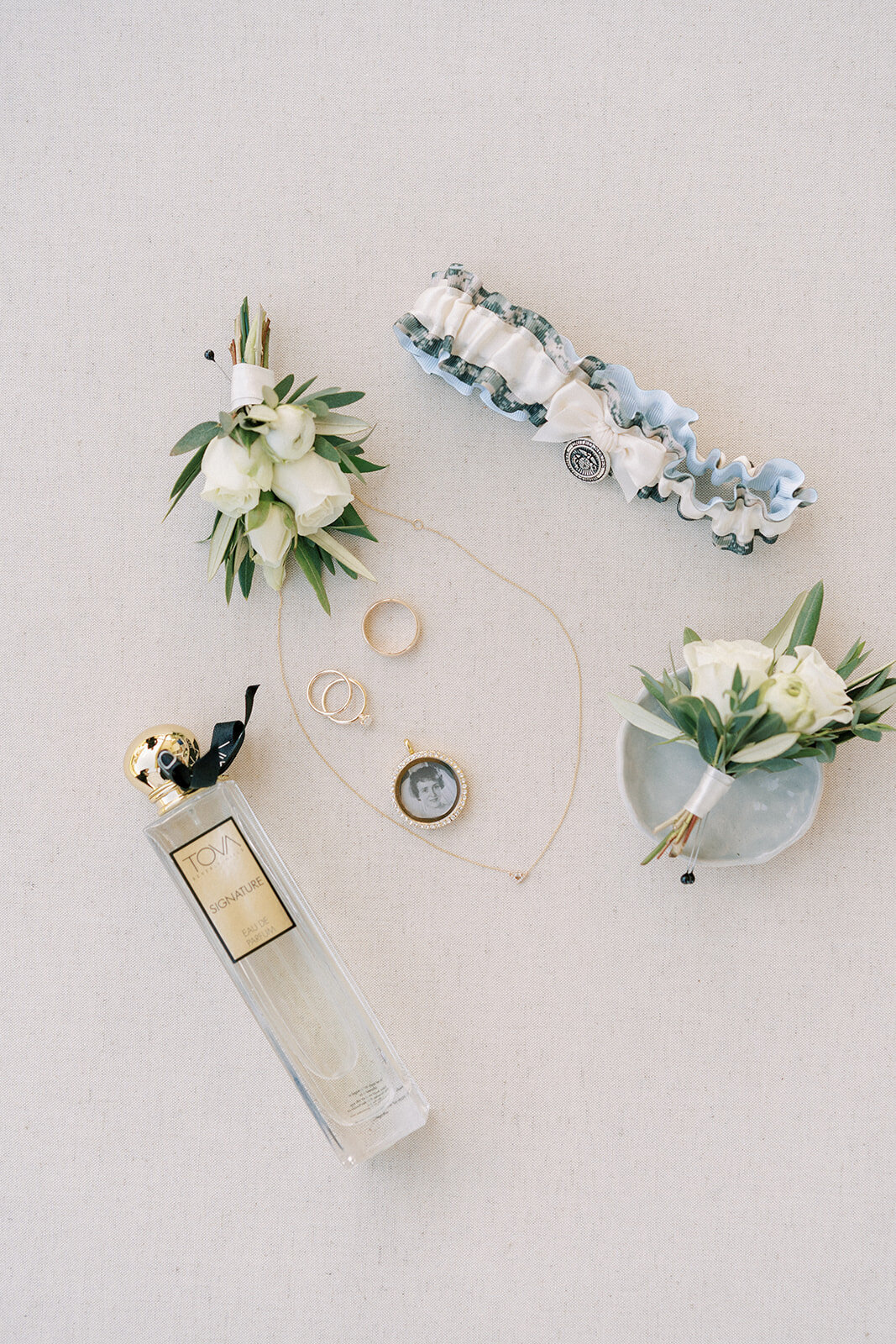 flat lay of white roses, wedding jewelry, and a perfume bottle