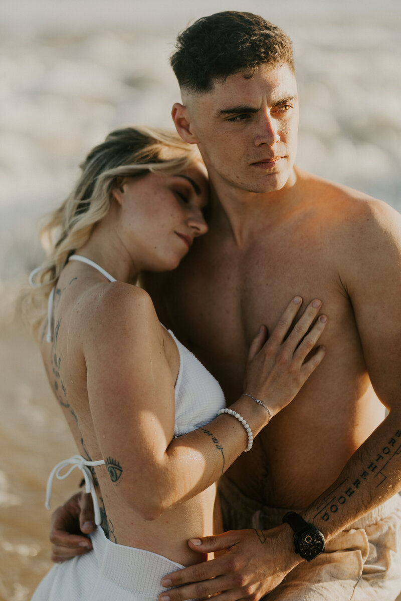 Femme en maillot de bain dans les bras de son chéri, reposant sa tête sur son épaule. Photo prise à la plage par Laura, photographe couple en Vendée.