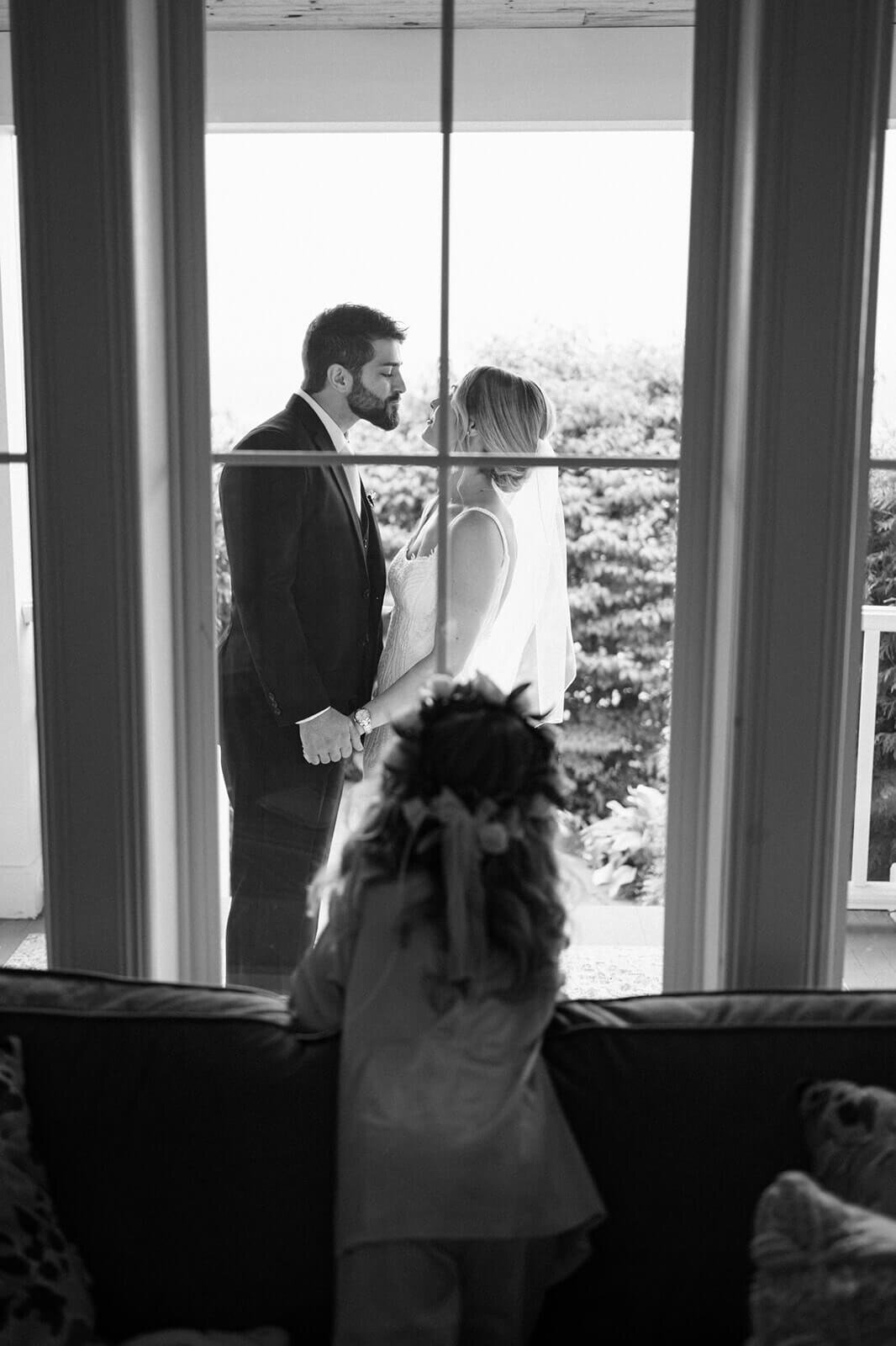 Girl looking out window at bride and groom as they have a first look