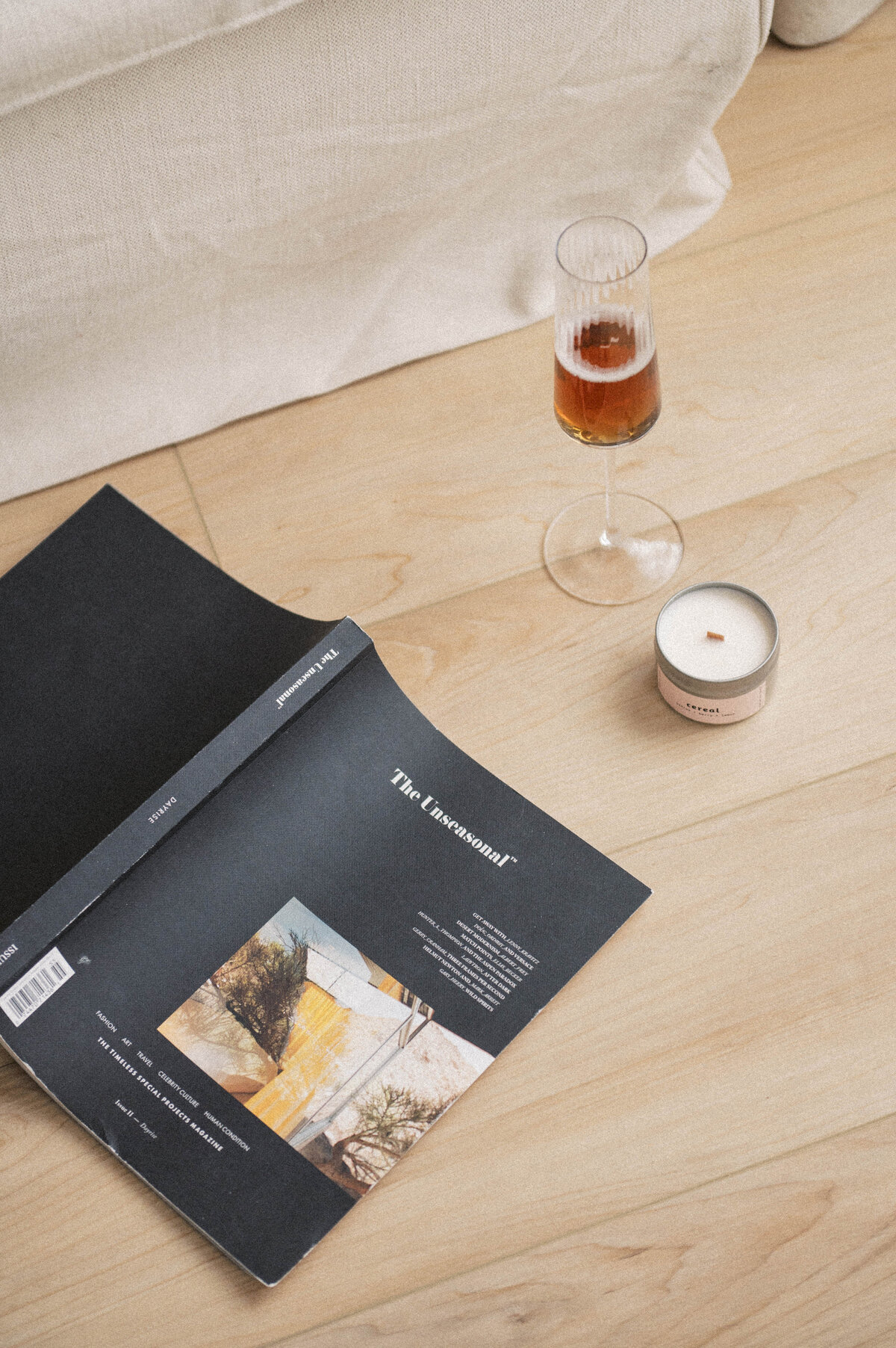 Black magazine art book laying open on the ground next to a candle and glass of wine