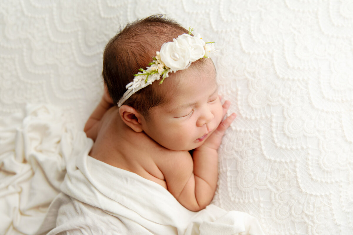 st-louis-newborn-photographer-baby-sleeping-on-white-crocheted-blanket-with-blanket-draped-over-her-wearing-a-flower-headband