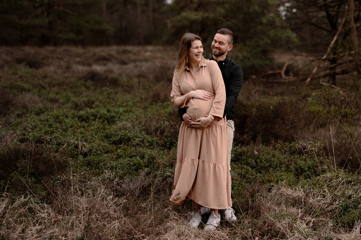 Man staat achter zijn zwangere vrouw en kijkt haar liefdevol aan terwijl zijn vrouw lacht