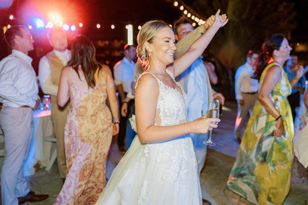 Bride dances joyfully with champagne in hand at her lively Cancun wedding reception.