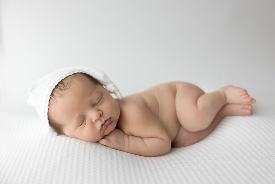 Newborn baby in sleepy cap sleeps on a white blanket.