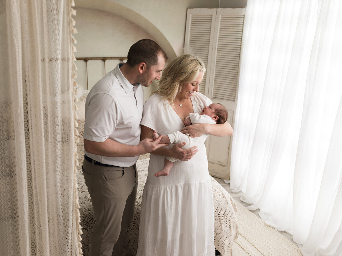 mom and dad holding newborn baby boy in white onesie for studio lifestyle session cleveland newborn photographer