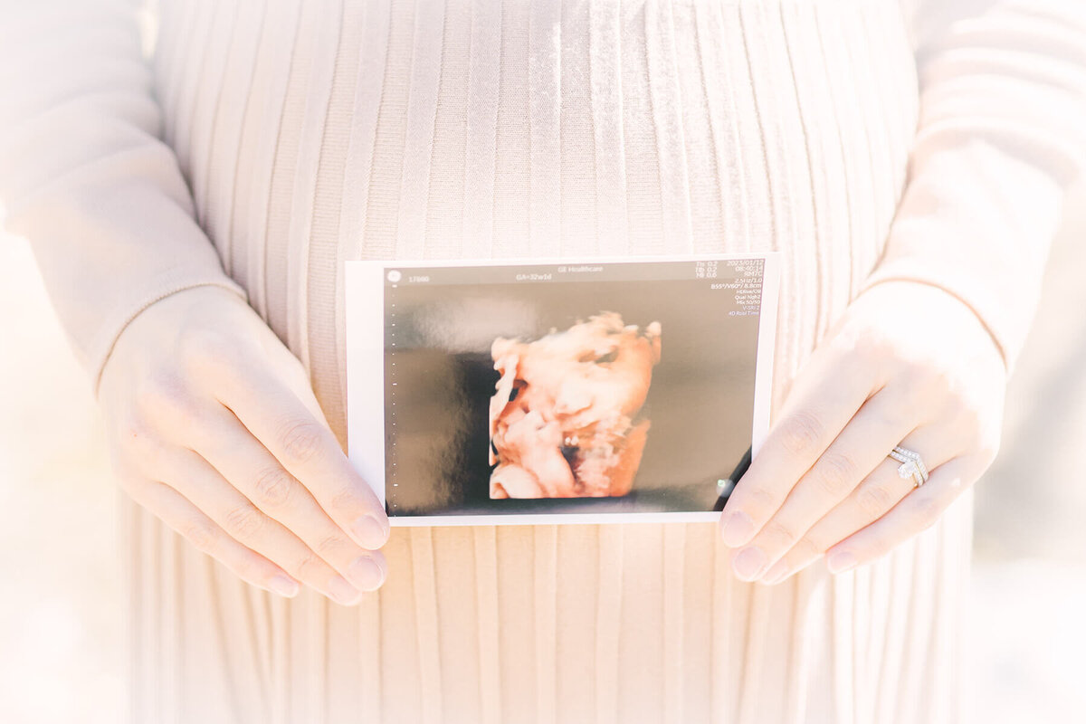 妊婦さんのおなかの前でエコー写真を持っているマタニティフォト。