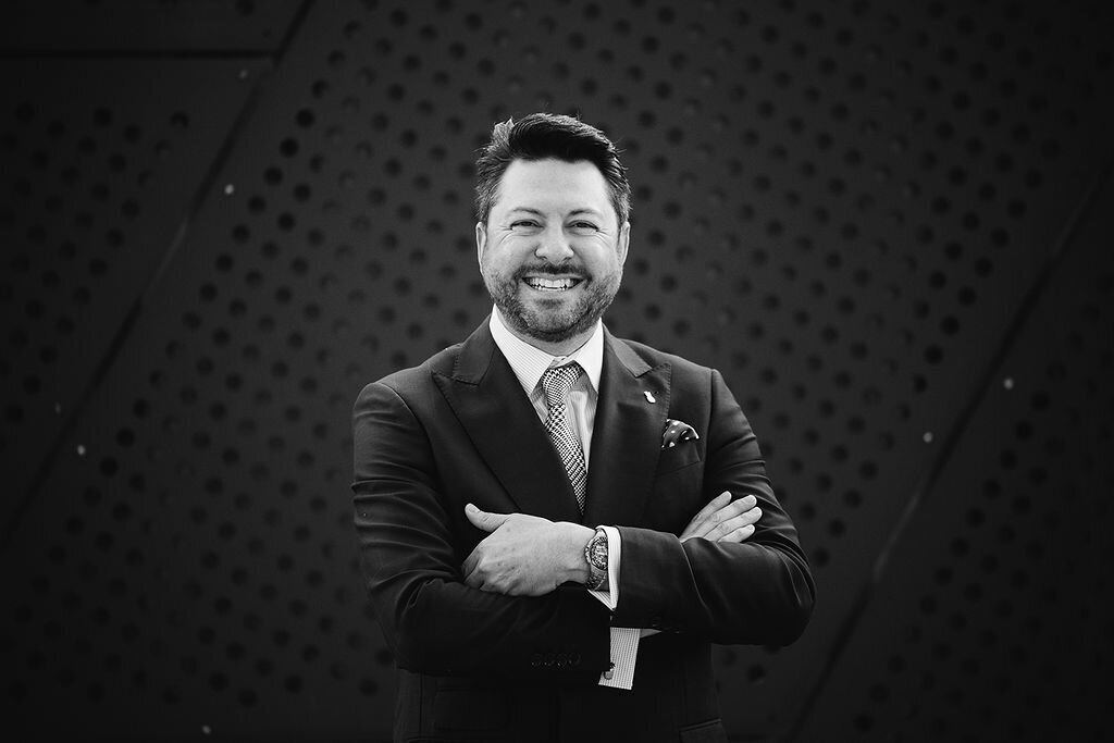 A man stands and smiles with his arms crossed.