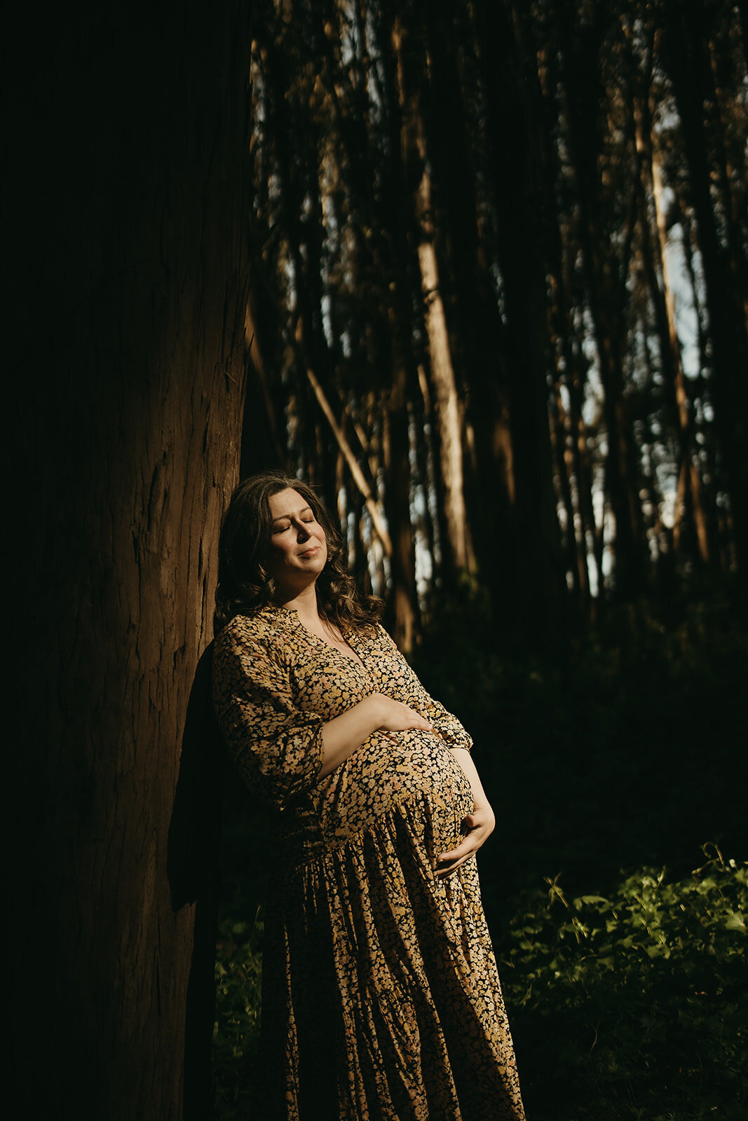 San Francisco pregnancy photo of mom in wooded area with eyes closed and snuggling belly