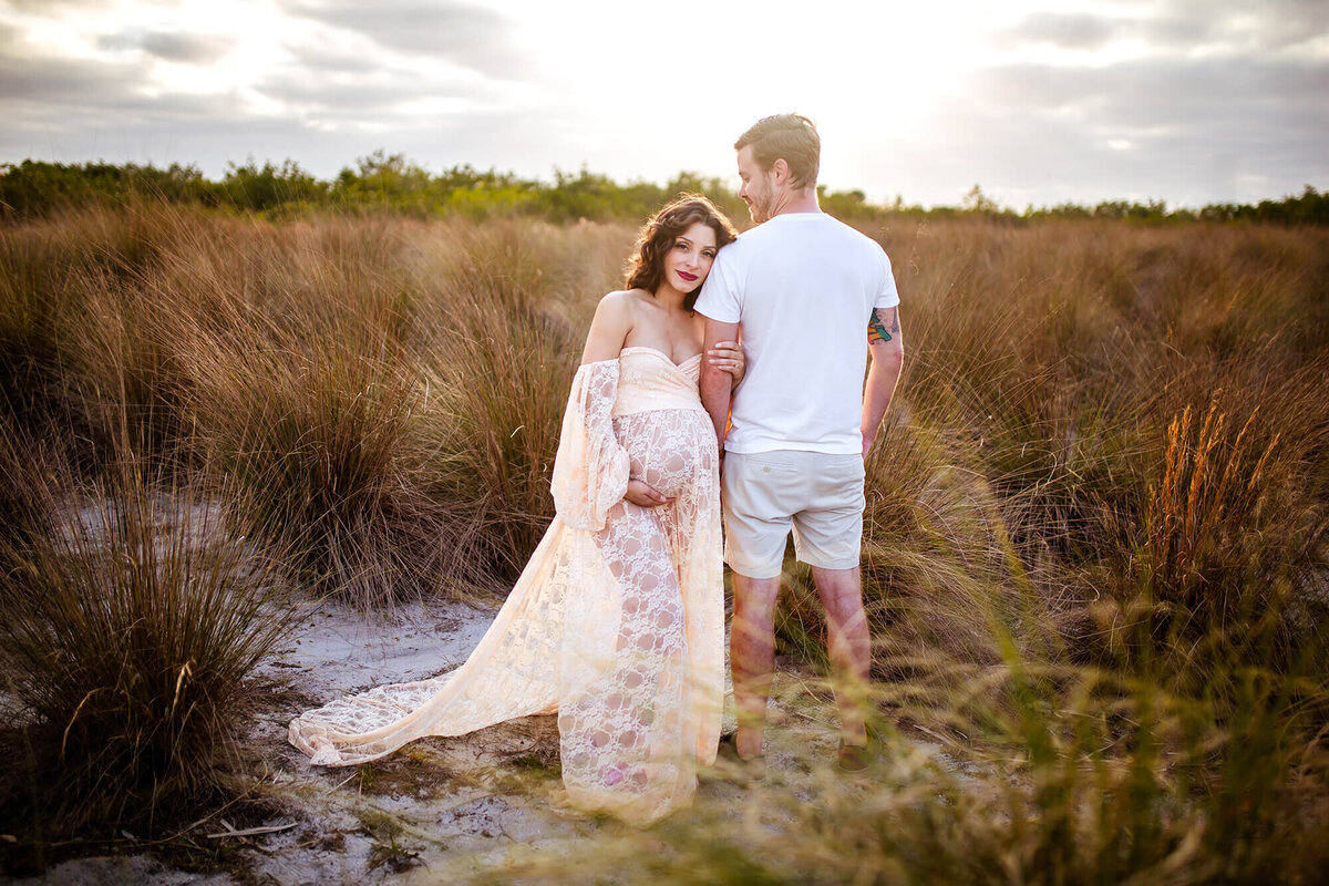 Mother cuddled on husbands arm and holding pregnant belly while he looks at her. Captured by Tampa Maternity Photographer Sarah Wyndham Photography