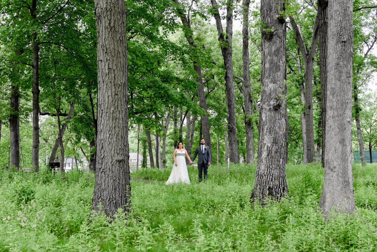 A bride and groom stand in the middle of a green forest