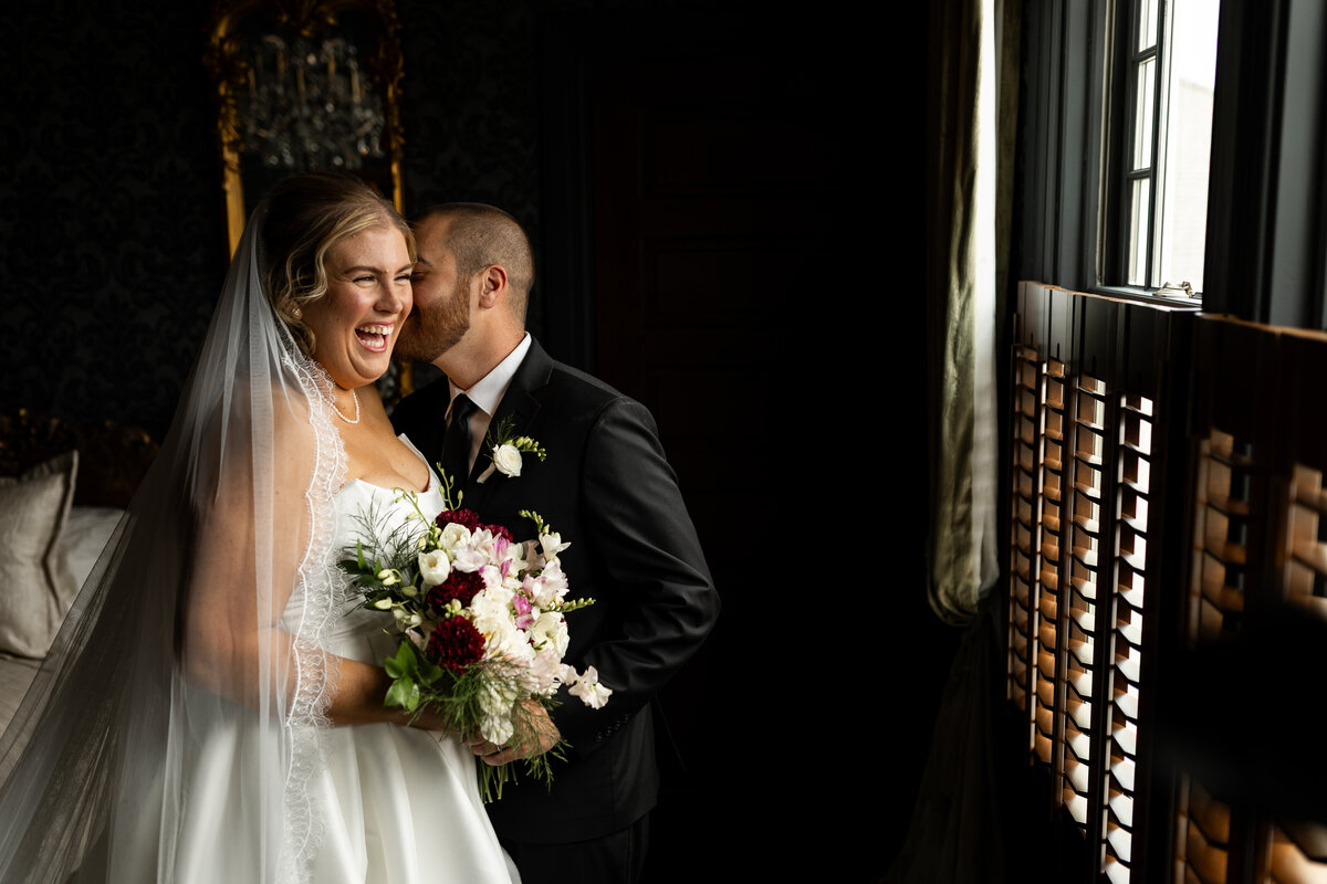 Groom whispering in his bride's ear, making her laugh.