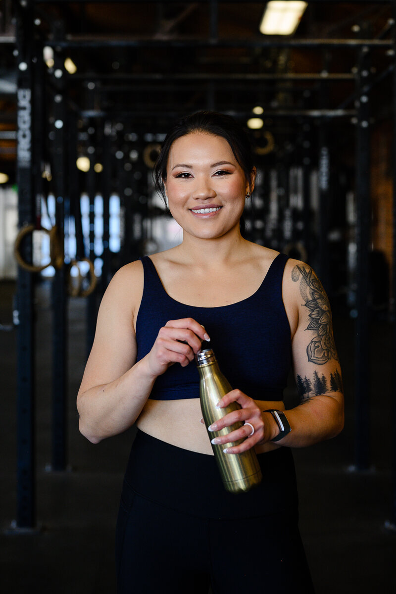 A commercial photographer in Denver takes a picture of a woman in a gym setting holding a water bottle and smiling at a brand photographer for her branding photos and brand photography session.